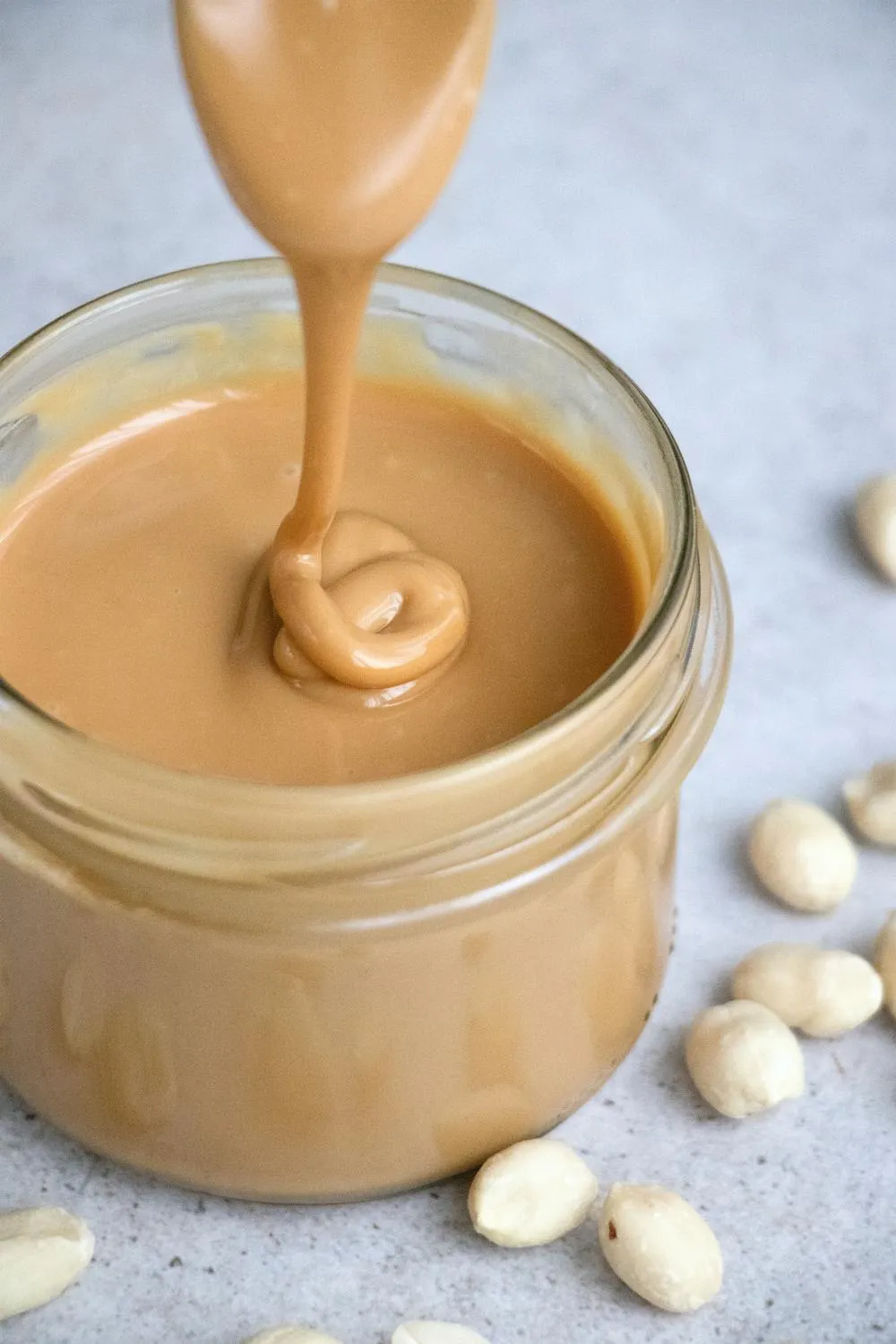 Peanut butter dripping from a spoon into a glass jar