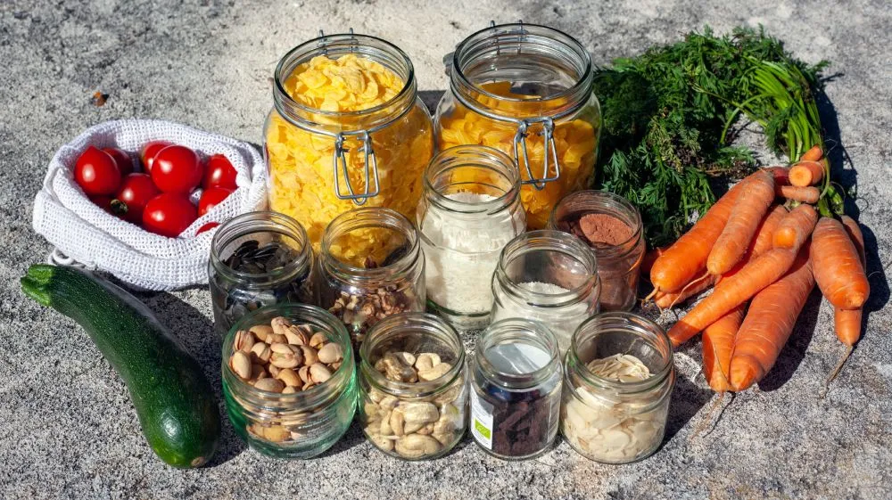 Glass jars of grains and legumes beside a zucchini, tomatoes and carrots