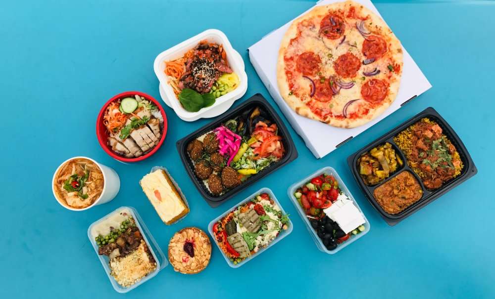 Assorted takeout meals and a pizza on a blue table, seen from above